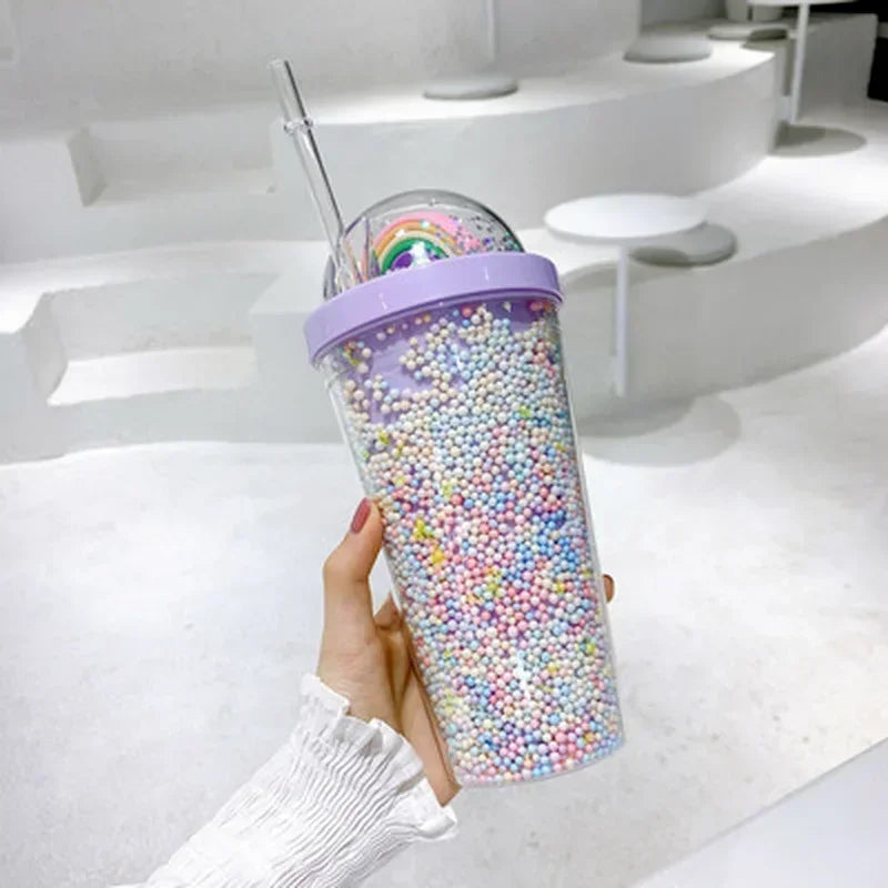 Kawaii tumbler with colorful beads and a rainbow design held by a hand in a white sleeve.