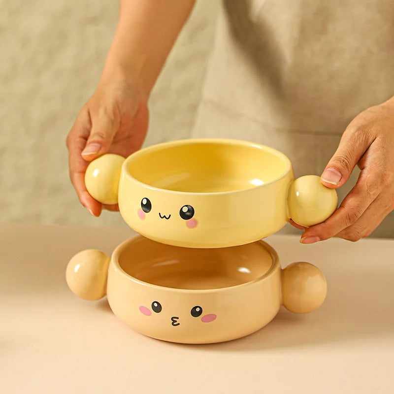 Two yellow ceramic kawaii ramen bowls stacked on top of each other with cartoon face, held by a person.