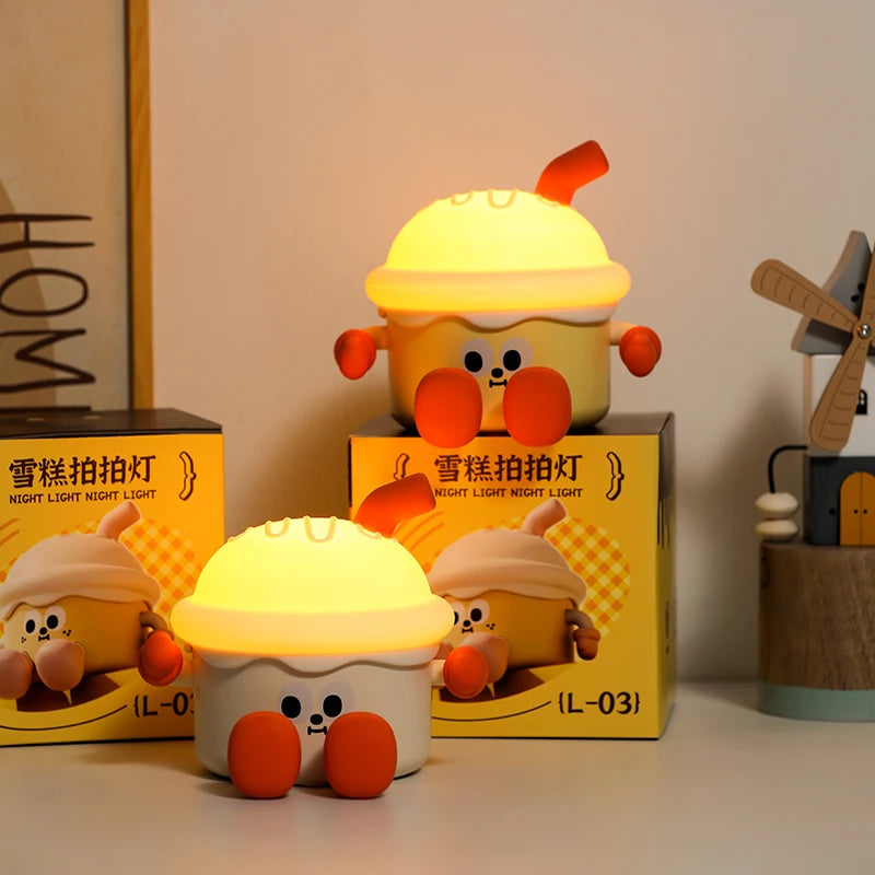 Yellow cartoon-like kawaii night light with red accents on a white surface, surrounded by boxes.