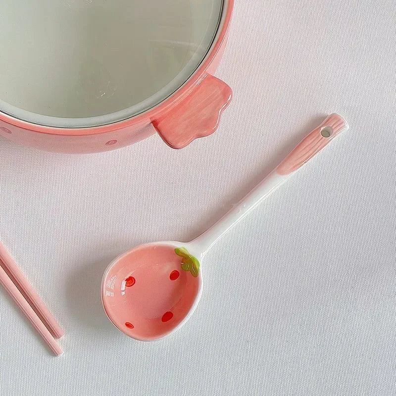 A close up of a strawberry designed kawaii bowl with a spoon next to it