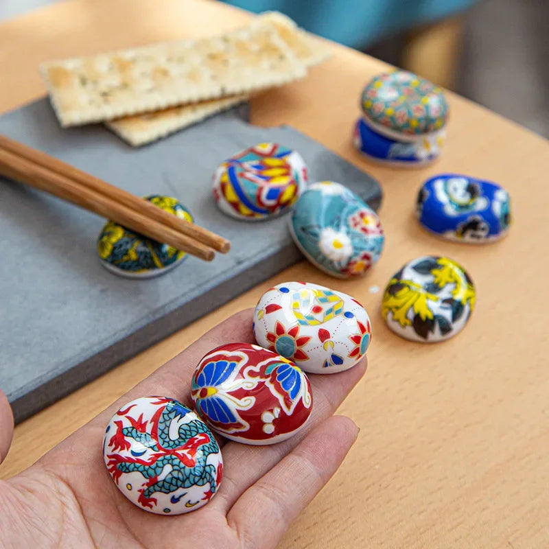 Colorful ceramic kawaii chopstick holders on a wooden surface with a hand holding one button.