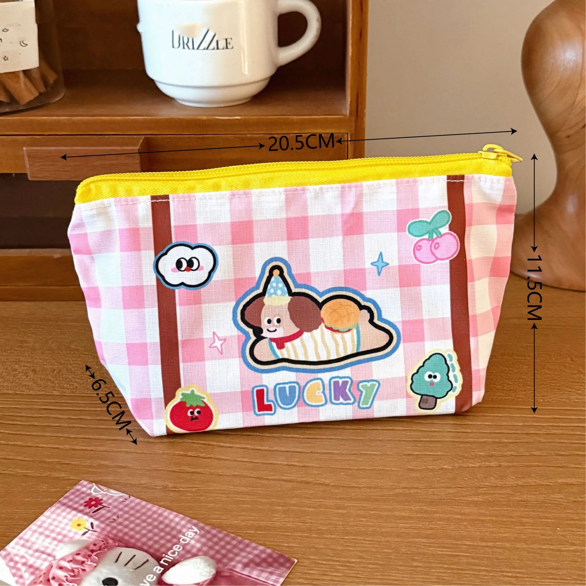 Pink checkered pouch with Kawaii cartoon character and 'Lucky' text on a wooden surface, with measurements indicated.