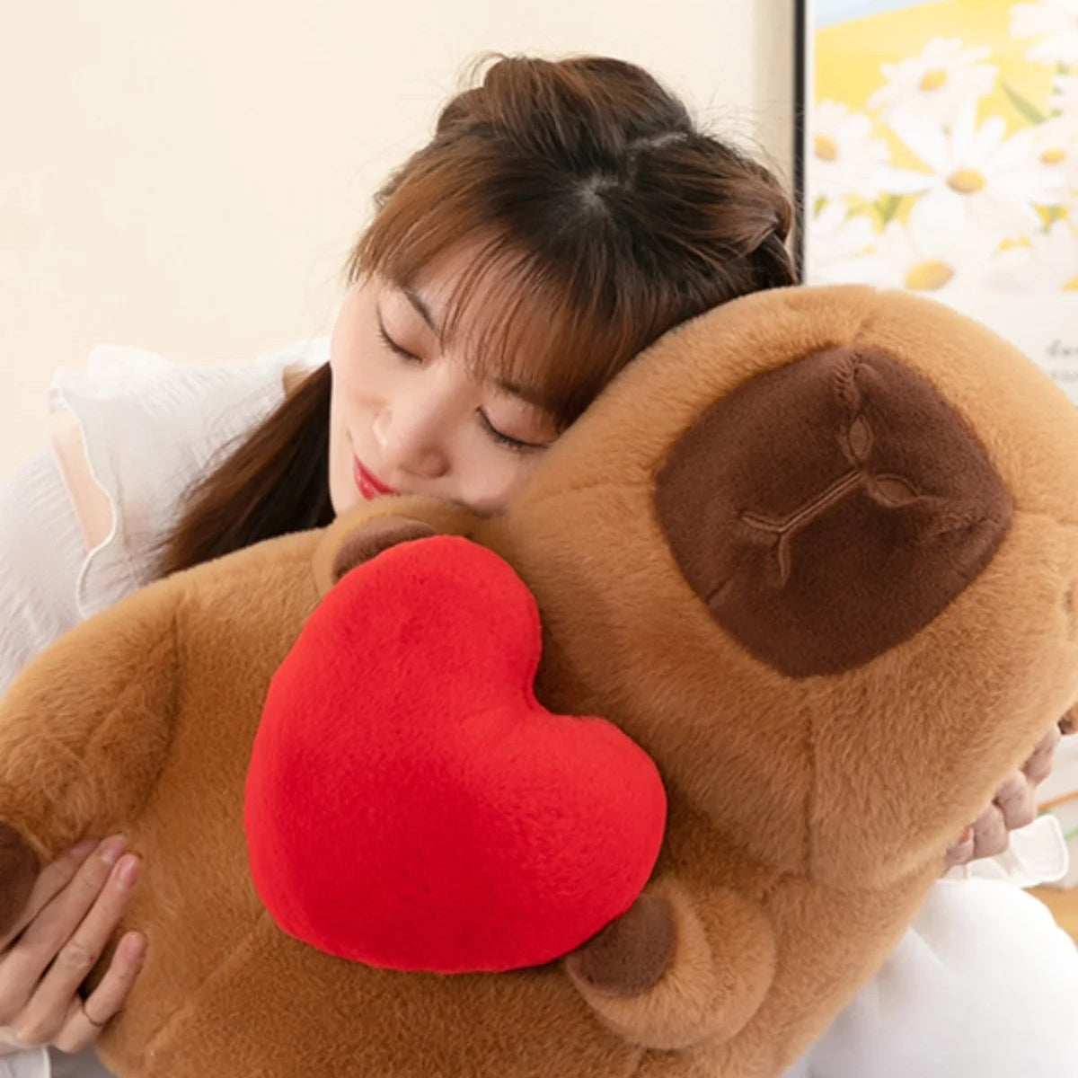 Person hugging a large brown kawaii plush toy with a red heart on a light-colored couch.