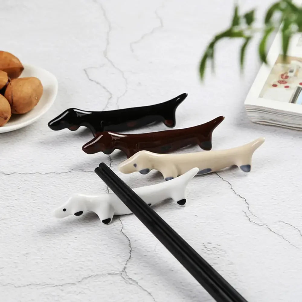 Set of four dog-shaped kawaii chopstick rests on a light gray surface with a plate of food and magazine in the background.