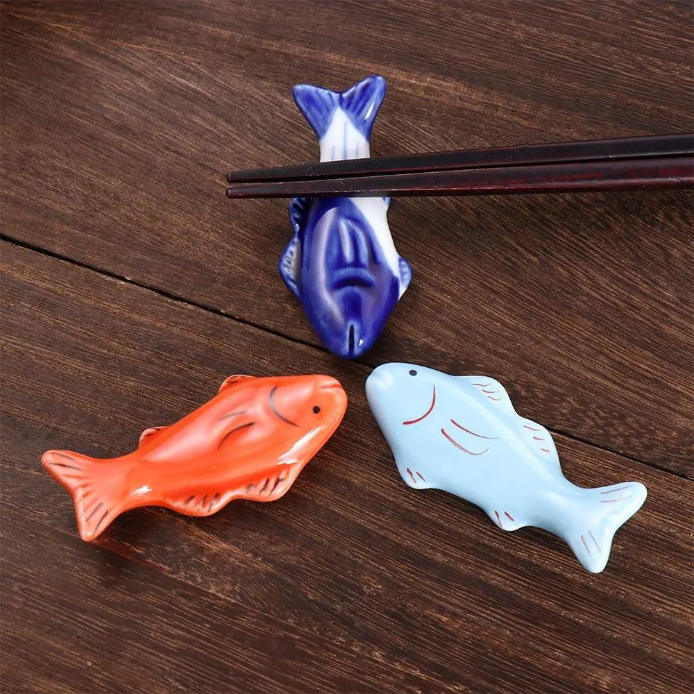 Three fish-shaped ceramic kawaii chopstick rests on a wooden surface with a pair of black chopsticks.