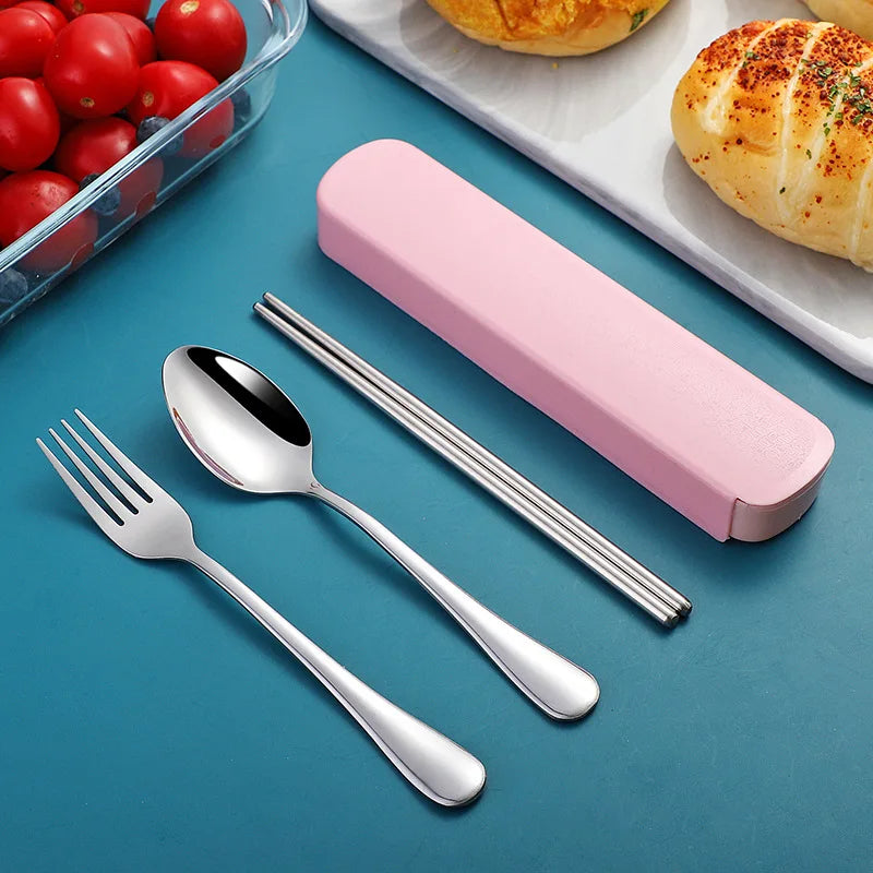 Silver kawaii utensils set with pink case on a blue surface, next to tomatoes and bread.
