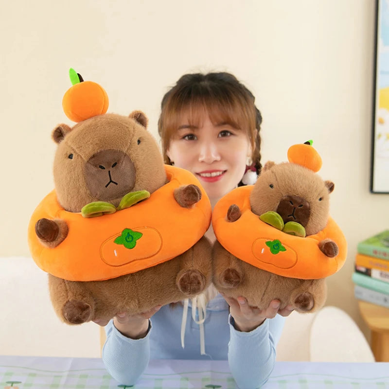 Person holding two kawaii plush toys resembling beavers in pumpkin costumes.