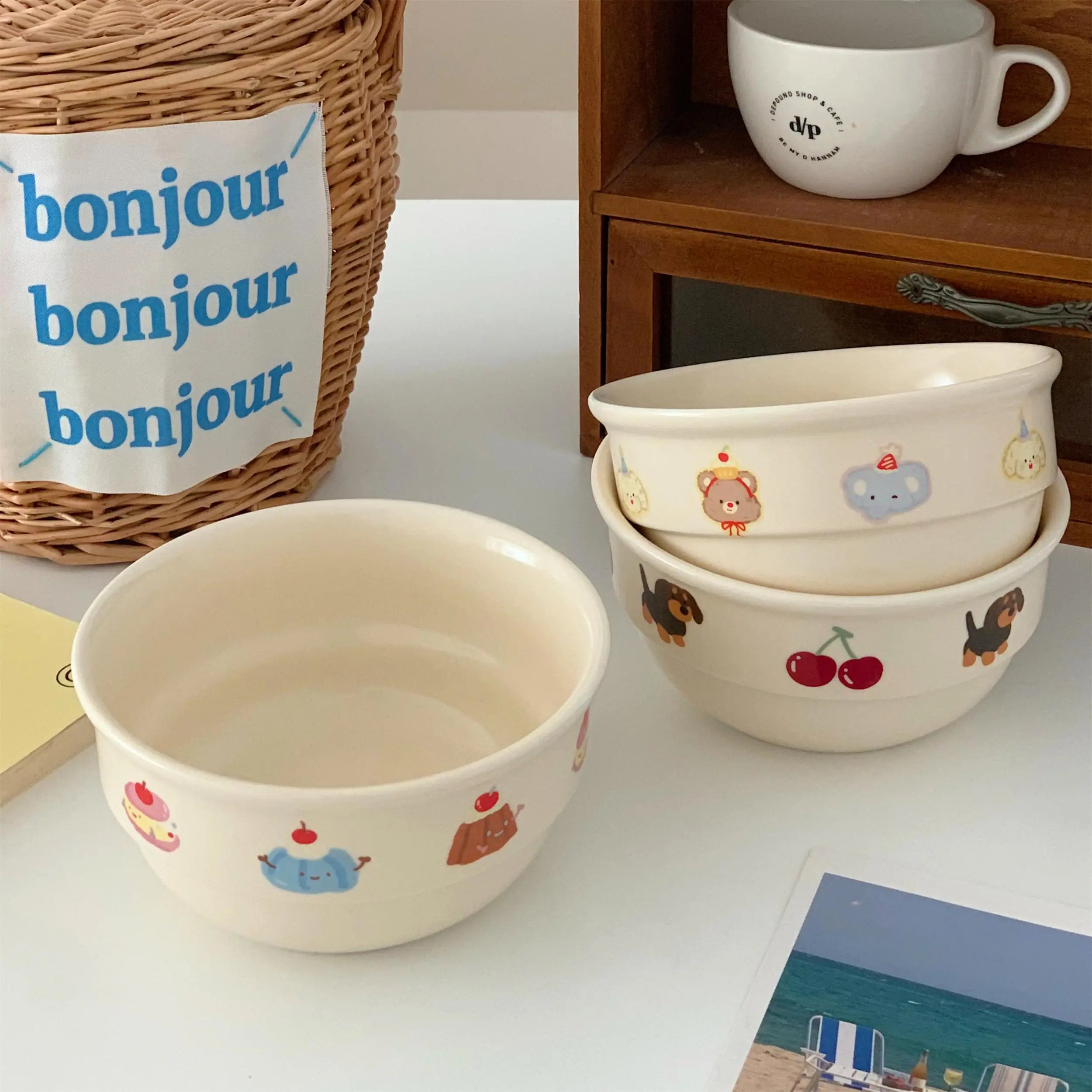 Set of ceramic kawaii ramen bowls with animal illustrations on a white surface, next to a wicker basket and a mug.