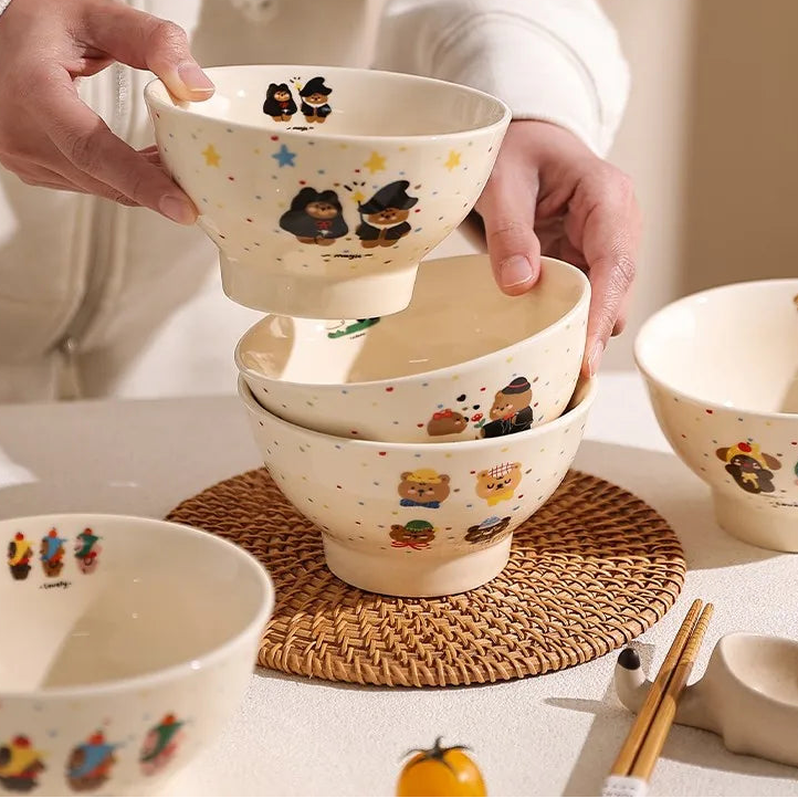 Person holding a stack of cartoon kawaii ramen bowls with bear designs on a table.
