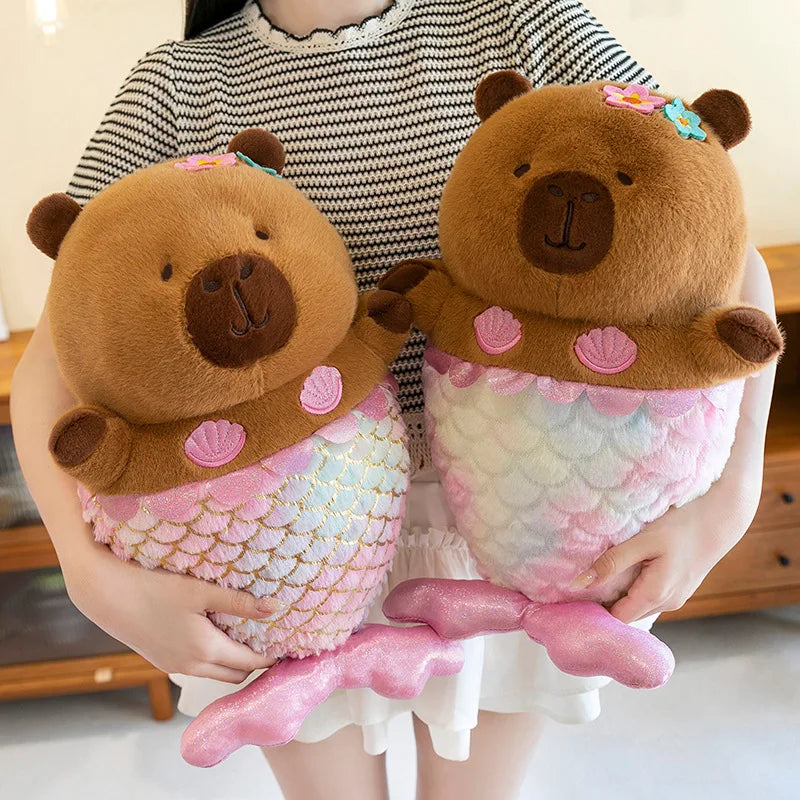 Two capybara plush toys resembling mermaid bears held by a person.