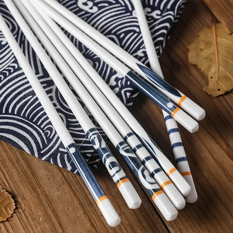 Set of white kawaii chopsticks with blue and orange design on a wooden surface with a patterned cloth.