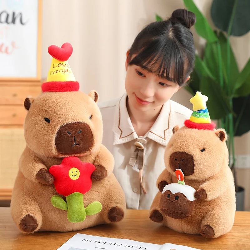 Person sitting at a table with two capybara plush toys wearing party hats.