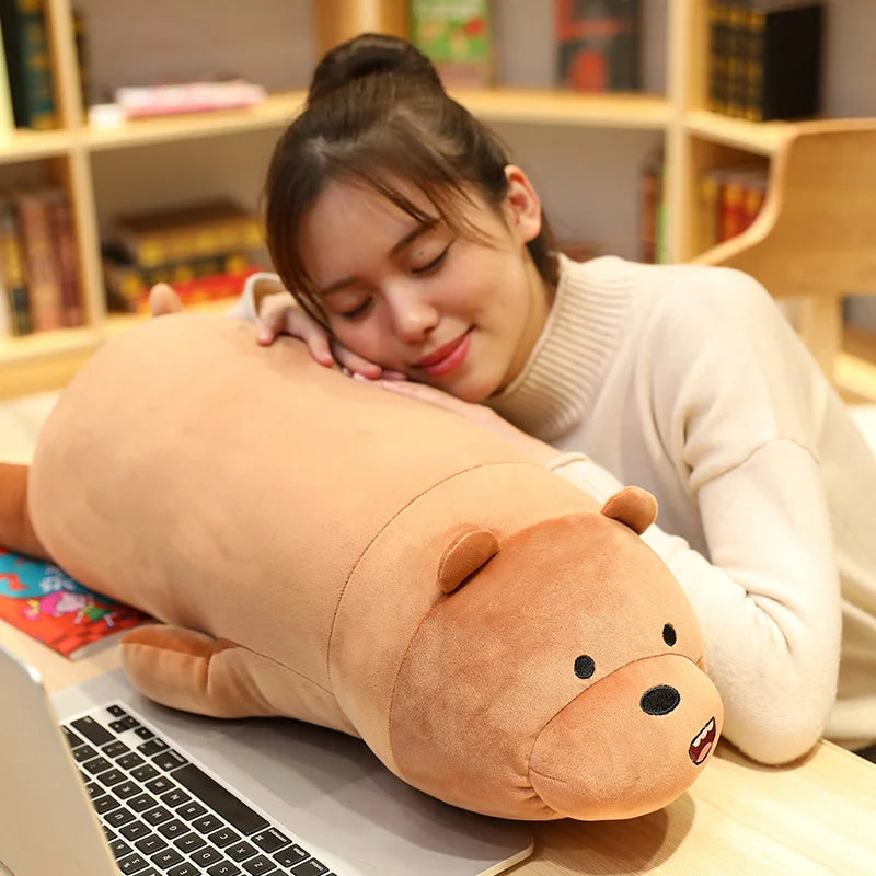 Woman lying on a large brown bear-shaped kawaii pillow at a desk with a laptop.