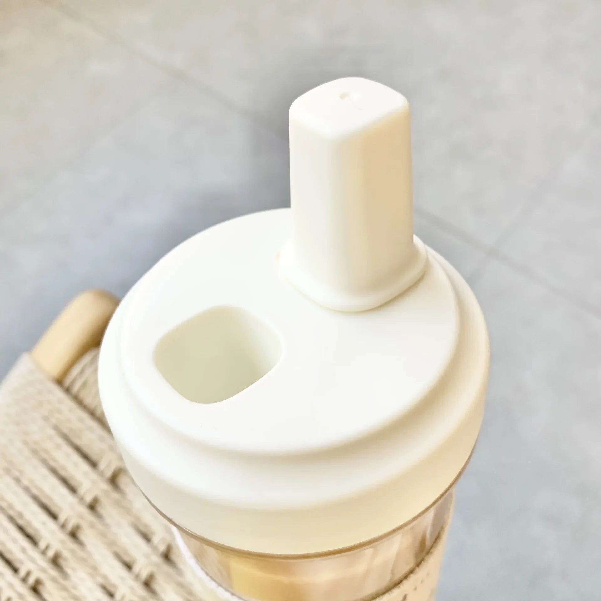 Close-up of a beige silicone straw lid on a kawaii water bottle with a wicker basket in the background.