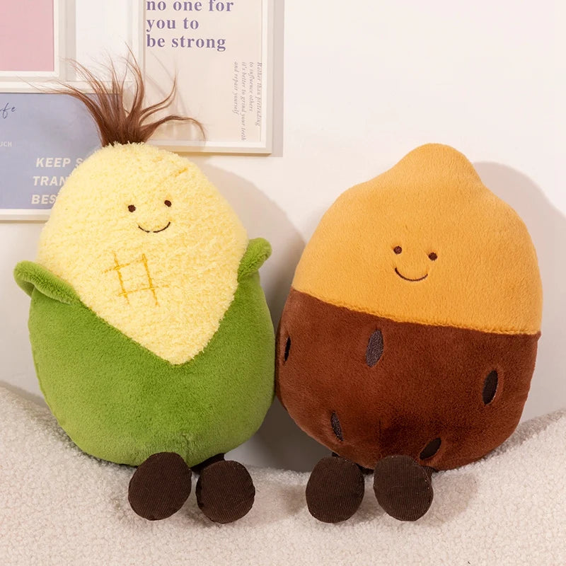 Two cute plush toy characters sitting side by side on a white textured surface. The left plush is shaped like a corn cob with yellow fuzzy exterior, green base, and brown tufted hair.