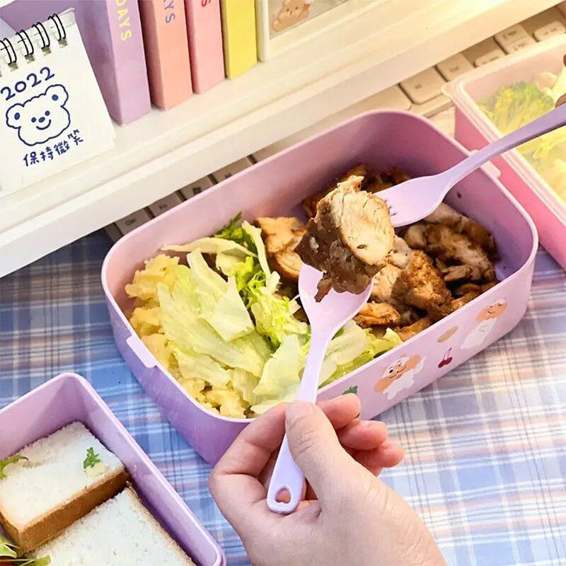 Pink kawaii bento box with food and a hand holding a spoon over it, on a checkered tablecloth.