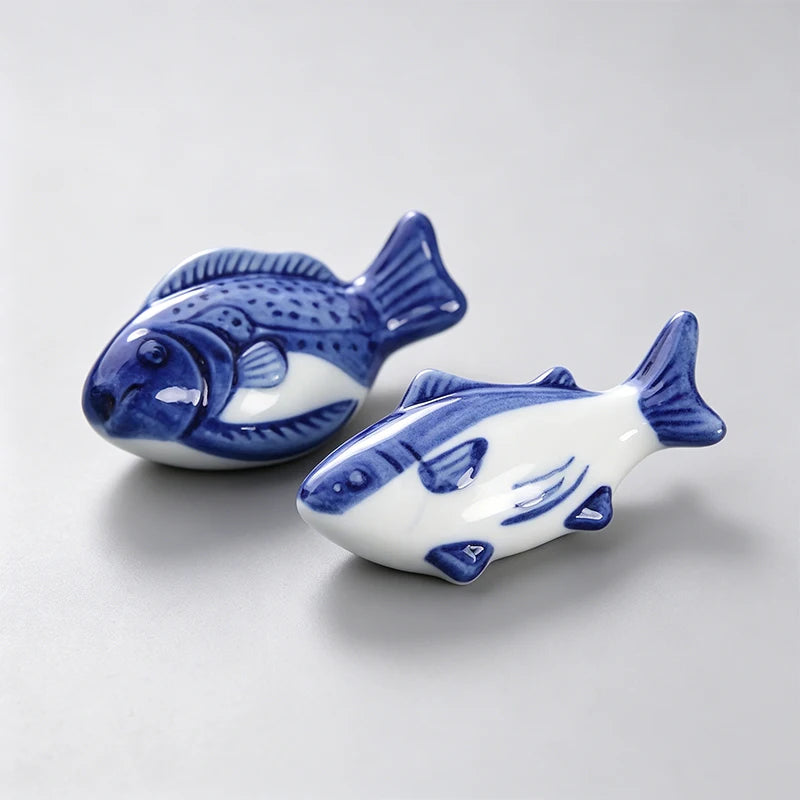 Two ceramic fish kawaii chopstick holders with blue and white design on a light gray background
