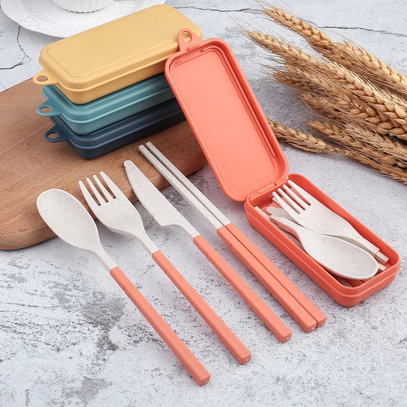 Set of kawaii utensils with orange handles in an open case on a light surface with wheat stalks.