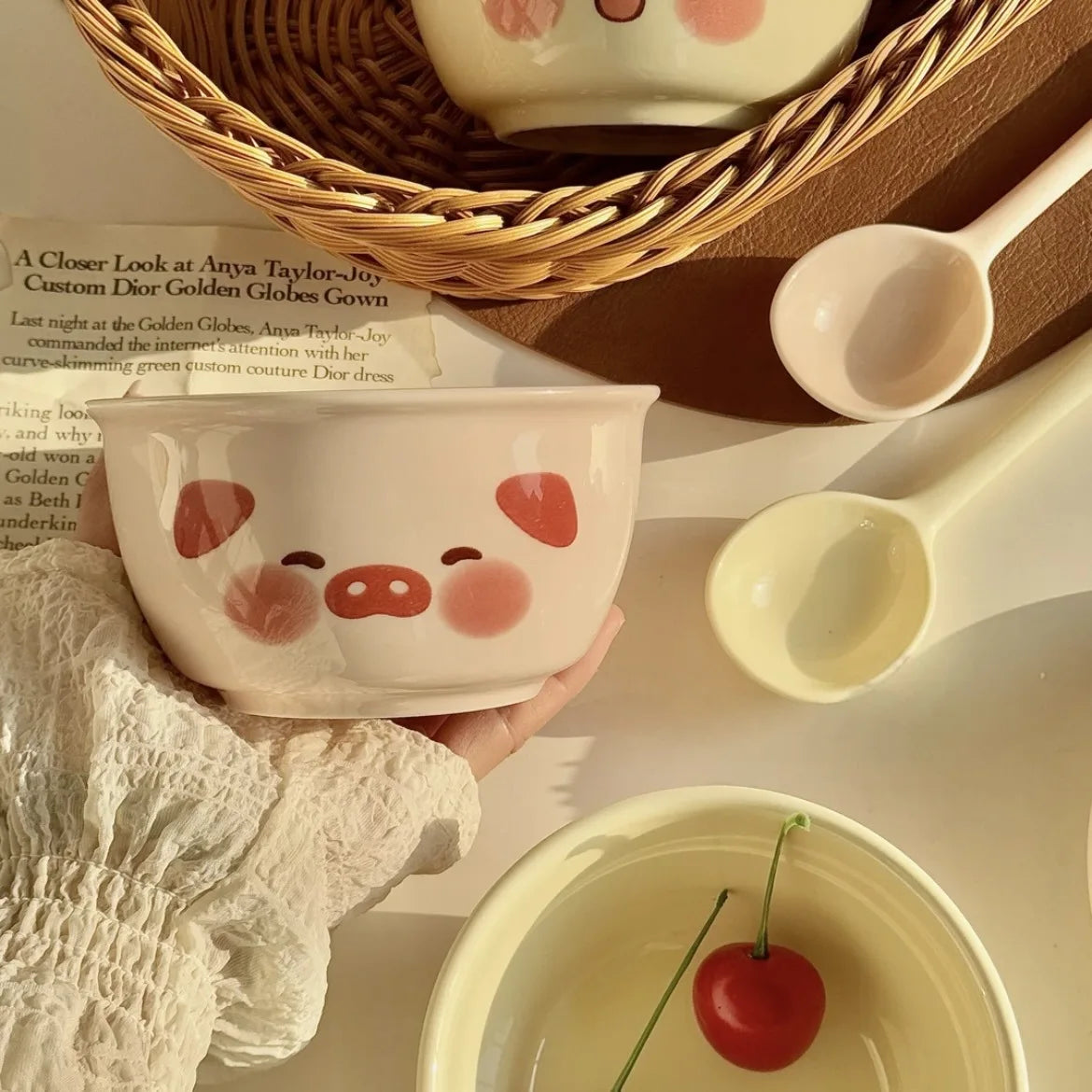Ceramic kawaii ramen bowl with a pig face design held by a person, surrounded by similar bowls and spoons.