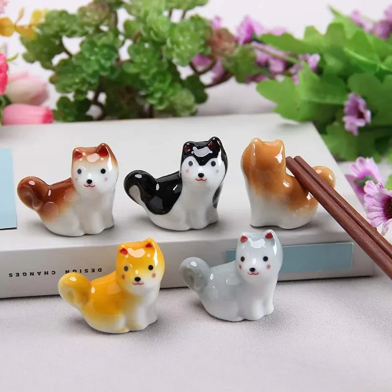 Set of four small kawaii dog figurines with chopsticks on a light surface with plants in the background