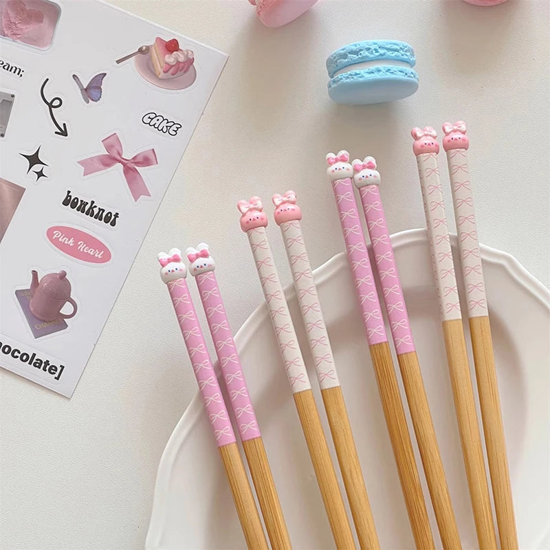 Set of pink and gold kawaii chopsticks with cat-themed tips on a white surface.