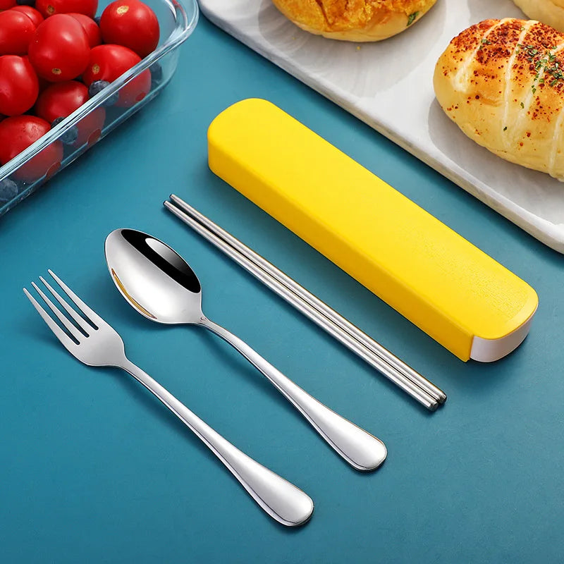 Silver kawaii utensils set with a yellow case on a blue surface, with tomatoes and bread in the background.