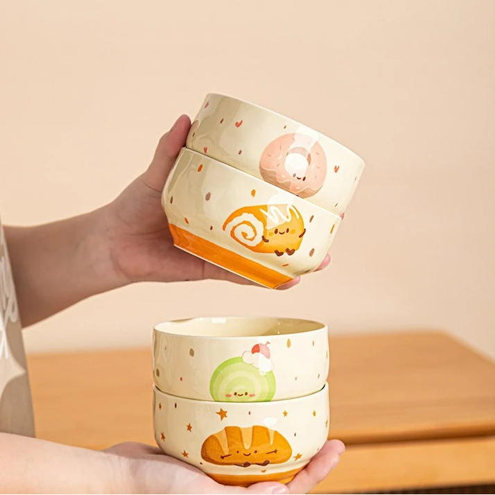Two stacked ceramic kawaii bowls with cartoon animal designs held by a hand against a beige background.
