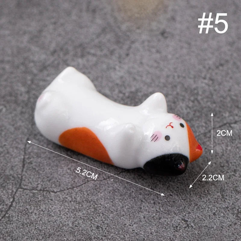 Small white and orange cat-shaped kawaii chopstick holders with measurements on a gray surface