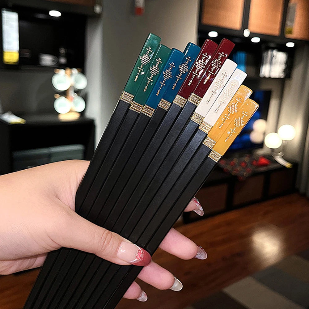 Hand holding a set of black kawaii chopsticks with colored handles in a blurred indoor setting