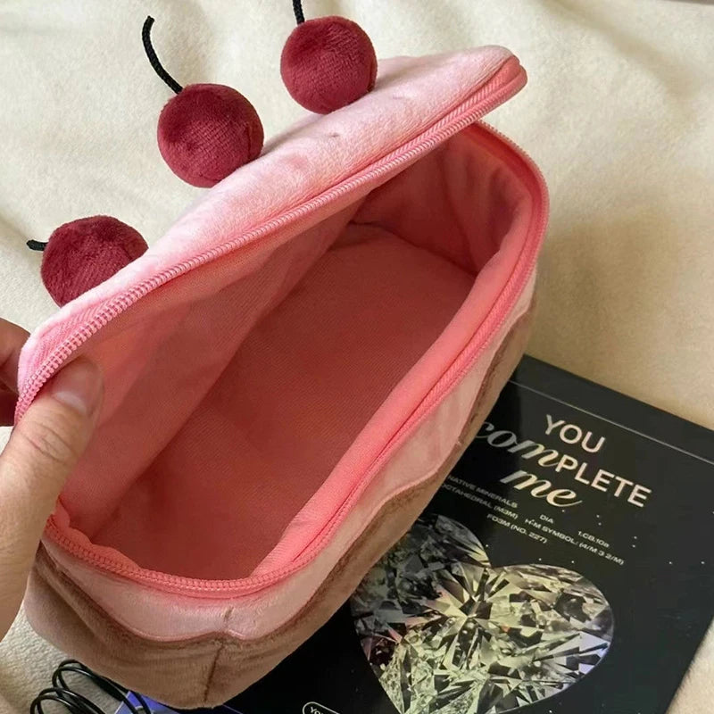 Pink pouch with kawaii red pom-poms held by a hand on a beige surface.