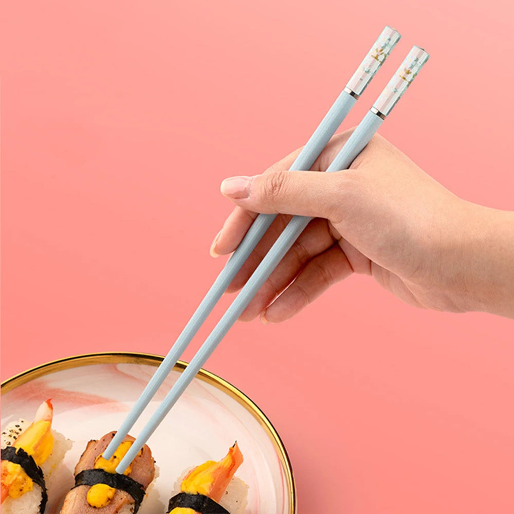 Hand holding light blue kawaii chopsticks over a bowl of sushi on a pink background