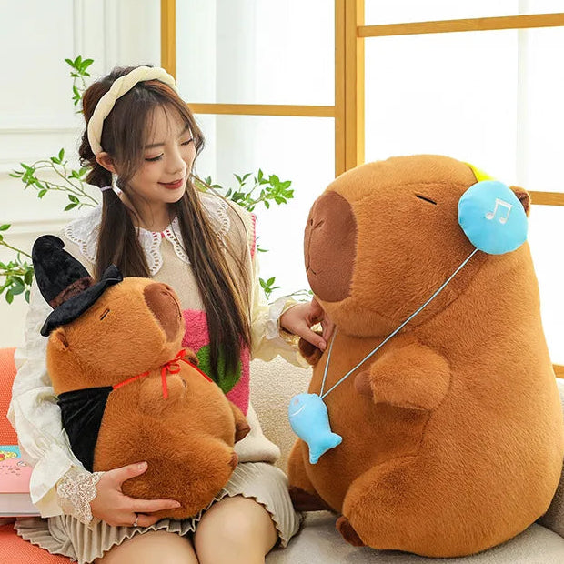 Woman sitting on a couch with two large capybara plush toys, one resembling a bear and the other a dog.