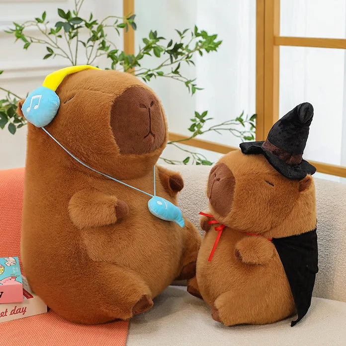 Two brown capybara plush toys sitting on a couch with a plant in the background.