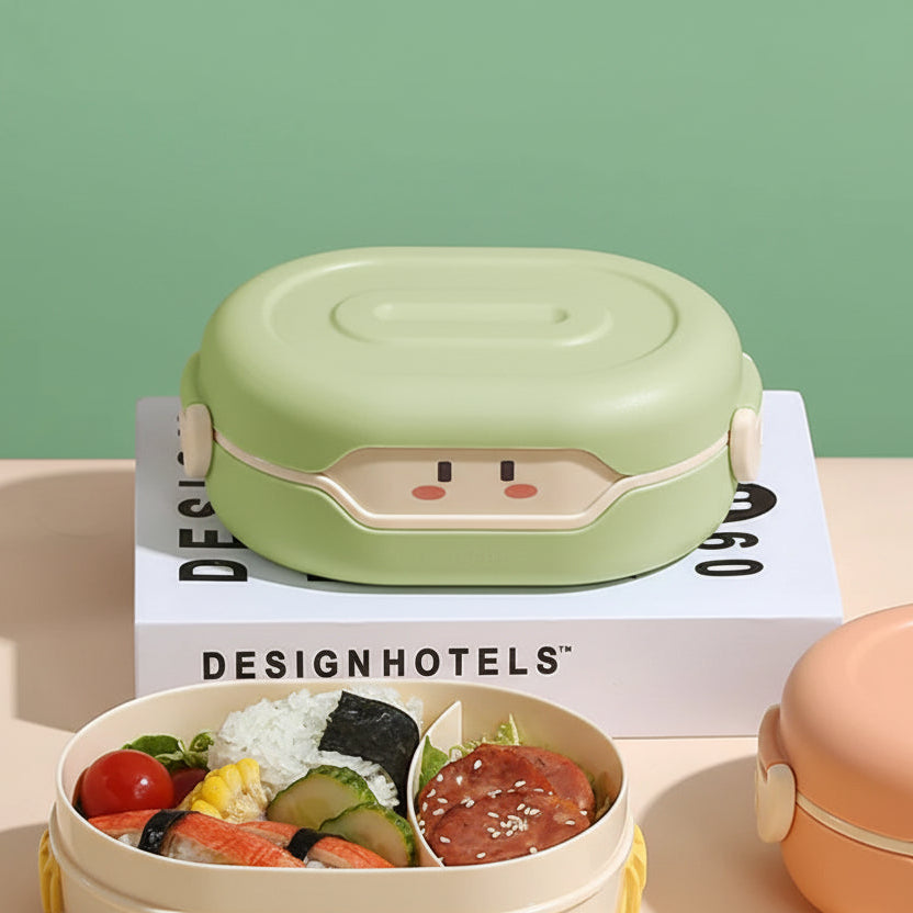 Green kawaii lunch box with cartoon face design on top of a 'DesignHotels' box, with a bento box containing food below.