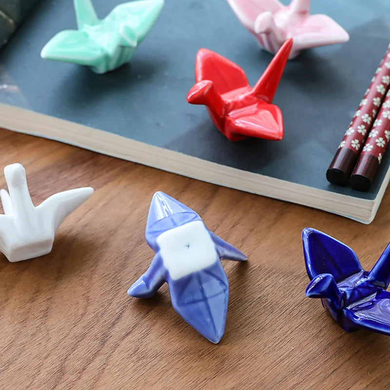 Colorful origami-style kawaii chopstick holders on a wooden surface with a notebook in the background.