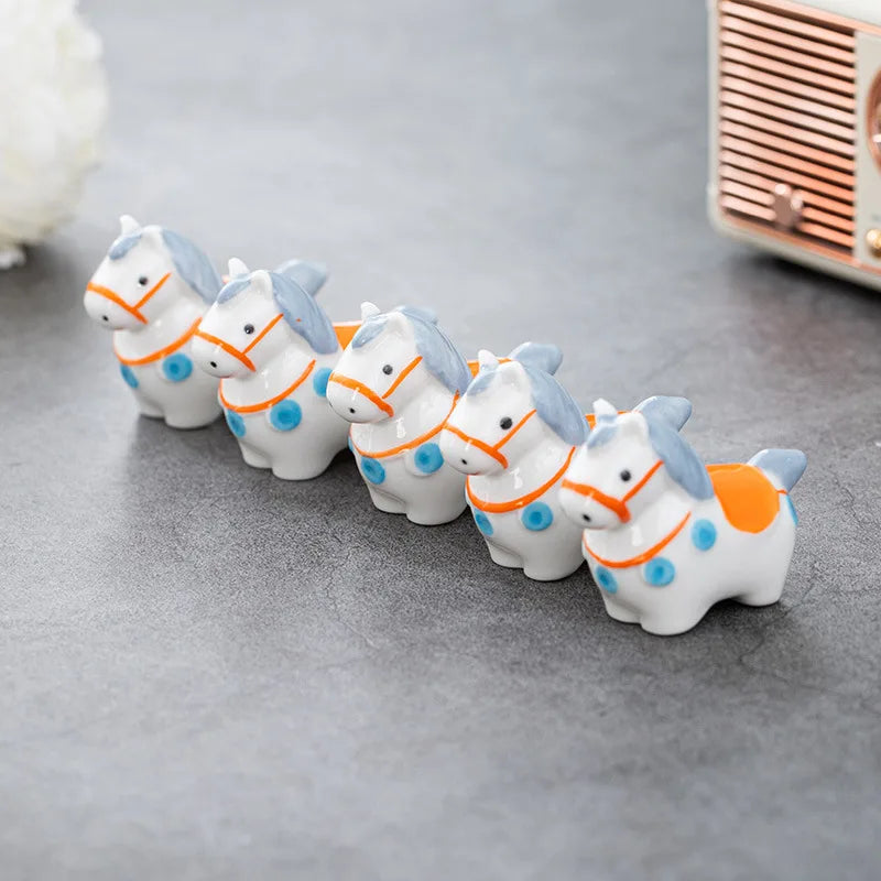 Five small horse kawaii chopstick holders in a row on a gray surface with a blurred background