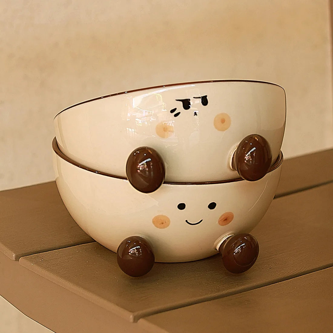 Two ceramic kawaii ramen bowls with cartoonish designs stacked on a wooden surface.