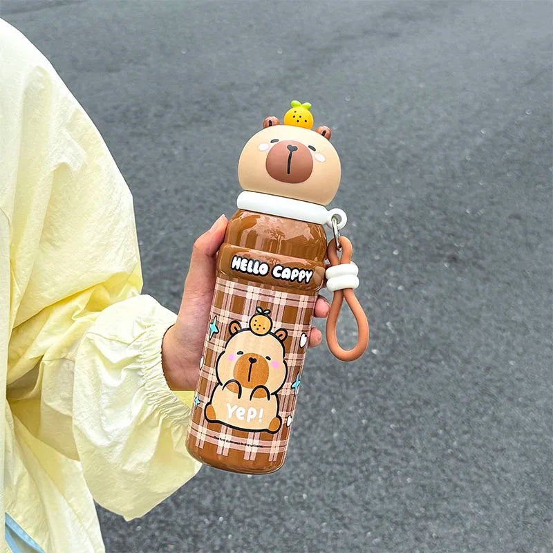 Person holding a cartoon bear-themed kawaii water bottle with a keychain on a gray pavement background
