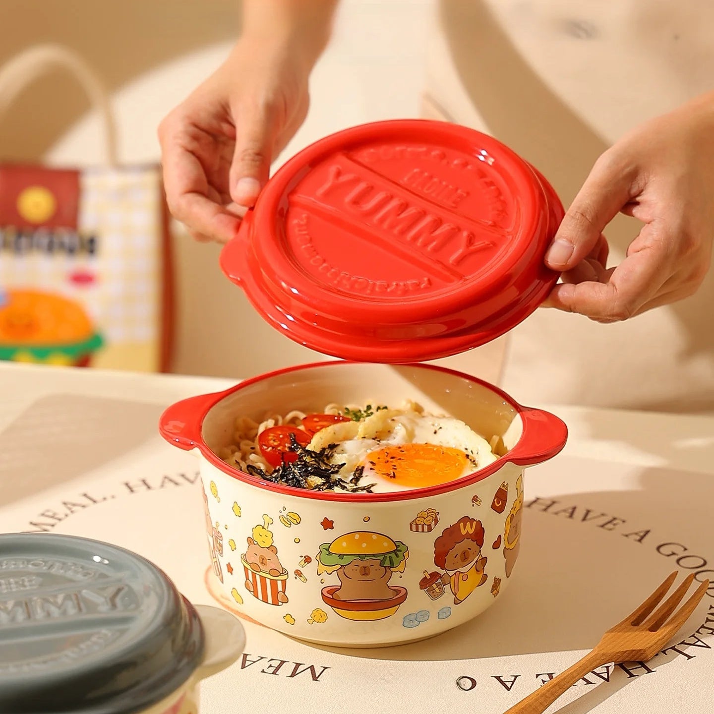 Person opening a red-lidded kawaii ramen bowls with cartoon designs on a table.
