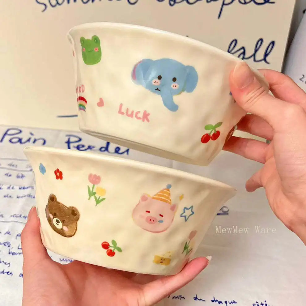 Two ceramic kawaii ramen bowls with animal illustrations held by a hand on a paper background.