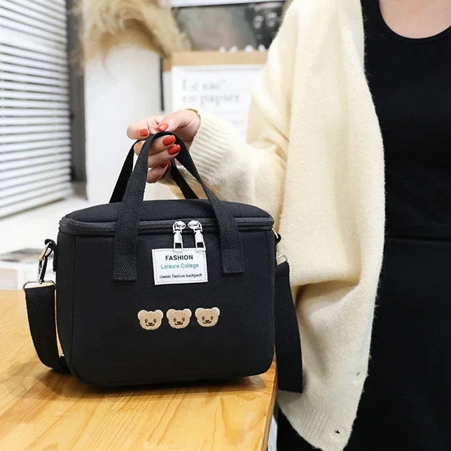 Person holding a black kawaii lunch bag with bear decorations on a wooden table.