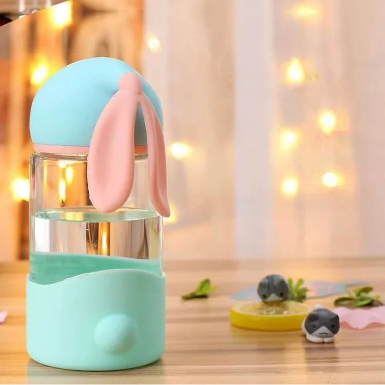 Cute kawaii water bottle with bunny ears on a wooden surface with decorative lights in the background