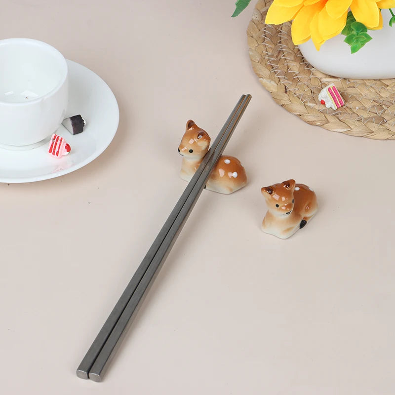Chopsticks on a beige surface with two small deer kawaii chopstick holders and a cup in the background.