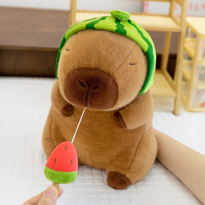Kawaii plush toy resembling a dog with a watermelon hat and watermelon slice in its mouth on a light surface.