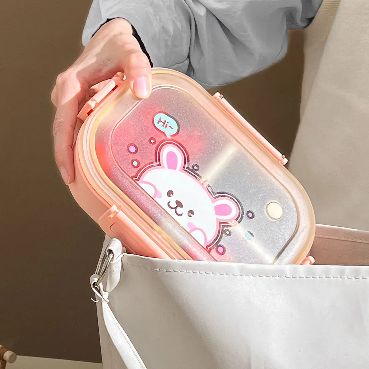 Person holding a kawaii pink lunch box with a cartoon design, featuring a bear and text.