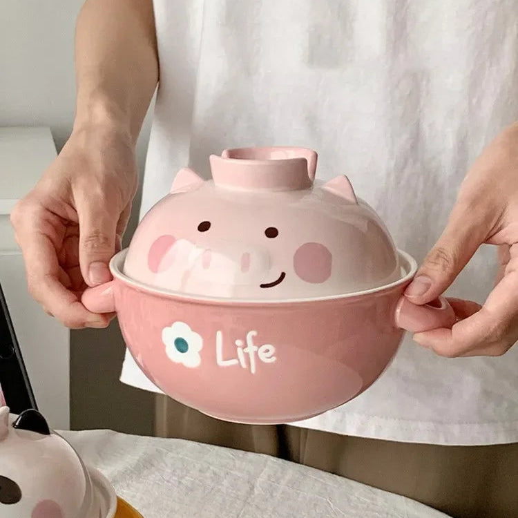 Person holding a pink kawaii ramen bowl with a pig design and 'Life' text, wearing a white shirt with text.