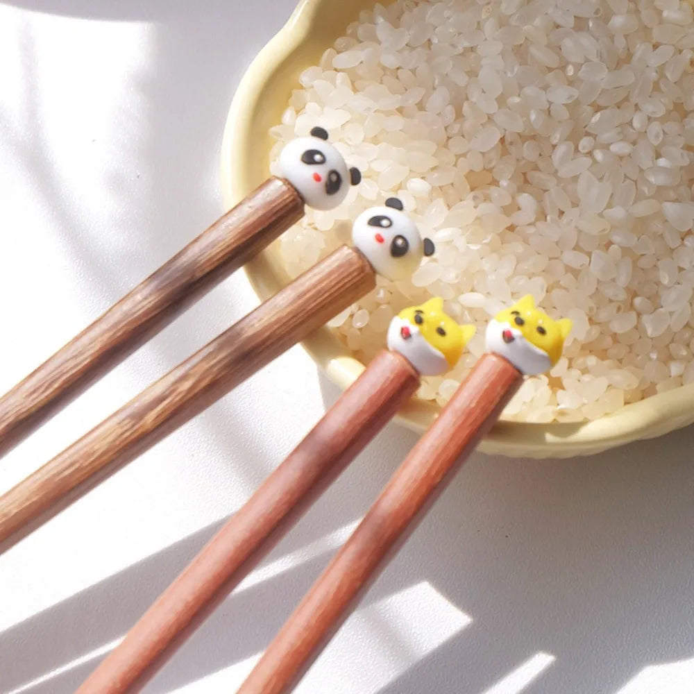 Wooden kawaii chopsticks with panda and cat-shaped ends on a bowl of rice.