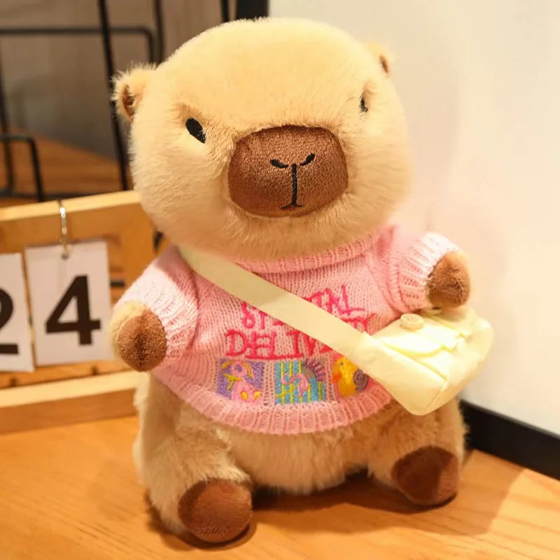 Kawaii plush toy bear wearing a pink sweater with colorful text and holding a yellow bag on a wooden surface.