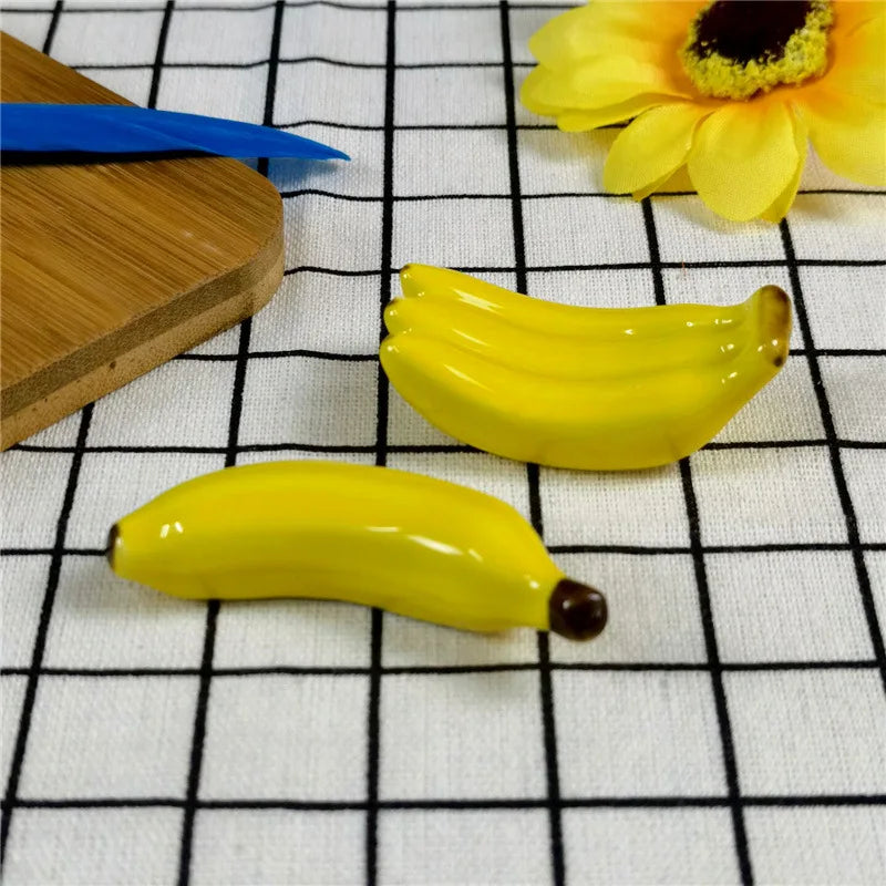 Two yellow bananas kawaii chopstick holders on a checkered tablecloth with a wooden cutting board and a yellow flower.