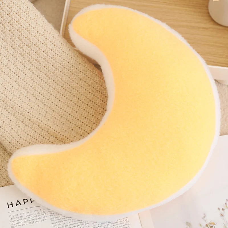 Yellow crescent moon-shaped kawaii pillow on a wooden surface with a textured fabric background.